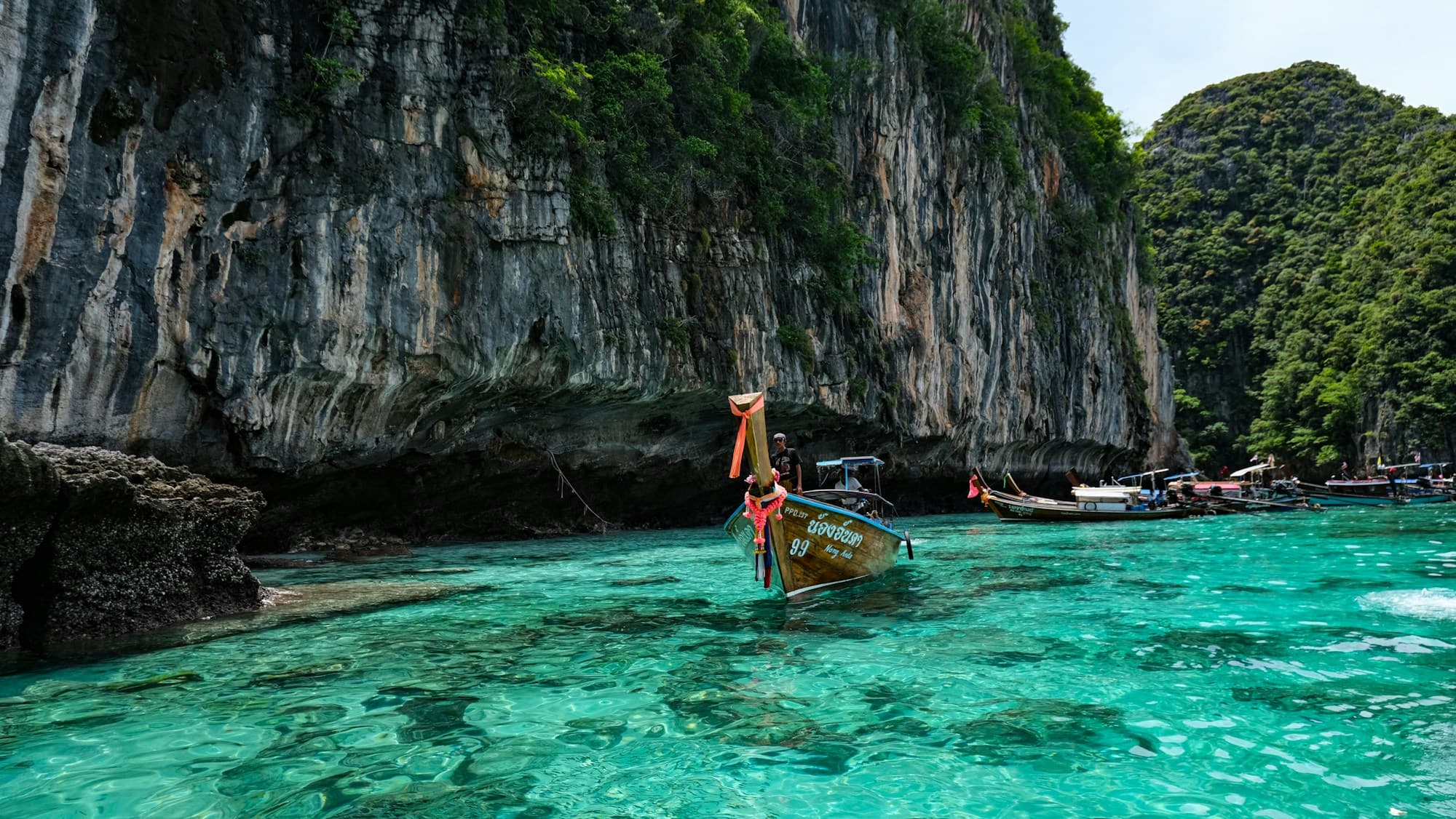 Longtail boats on turquoise water beneath limestone cliffs in Thailand